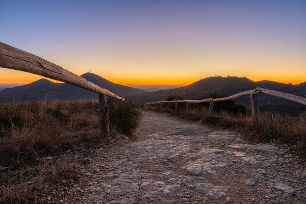 Hiking trail with a wooden fence overlooking a hillside panorama at sunset.