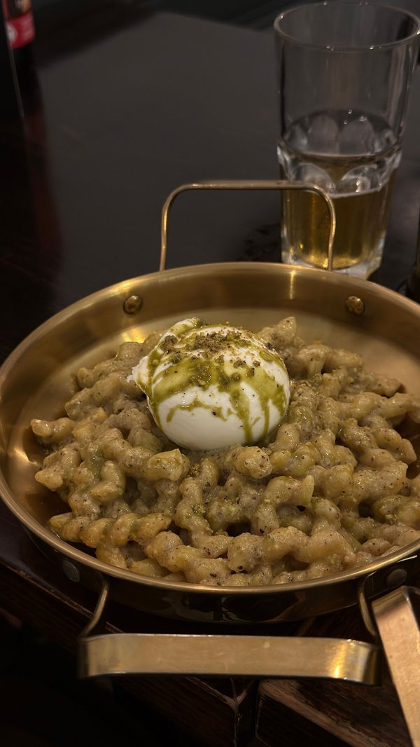 Piatto di pasta italiana con burrata e pesto servito in una padella dorata, tipico di una trattoria a Bologna.