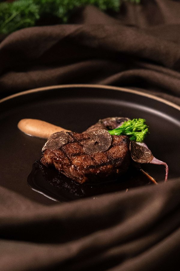 Piatto gourmet con filetto di carne, tartufo e verdure su un piatto nero, presentato elegantemente.
