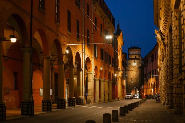 Portici illuminati di Bologna di notte con edifici storici e una torre sullo sfondo.