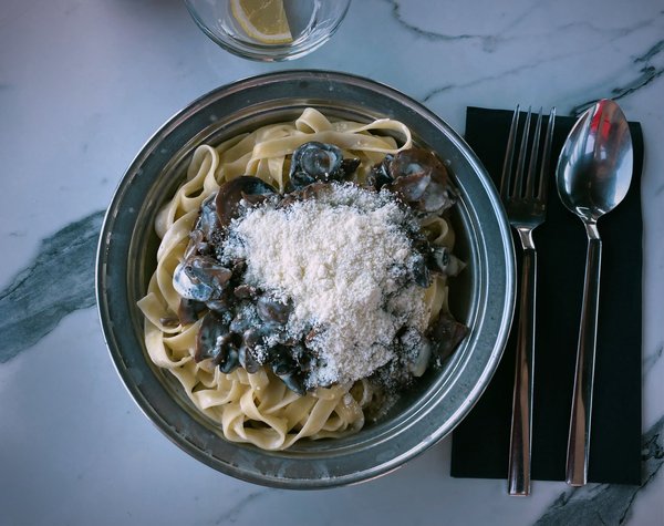 Tagliatelle con funghi e parmigiano servite in un piatto di metallo su un tavolo di marmo.