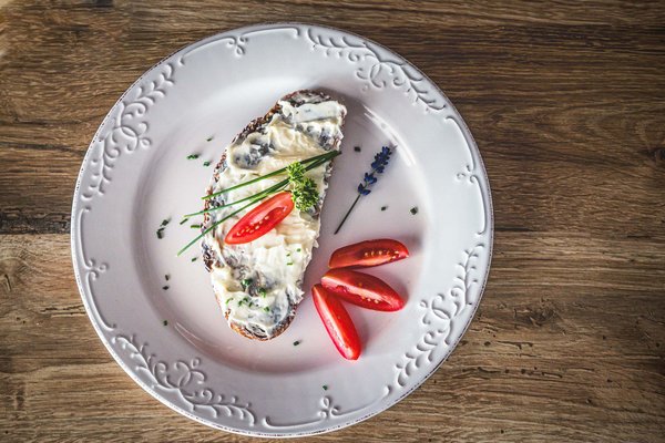 Piatto di pane con crema, pomodorini e decorazioni su un piatto bianco decorato, su un tavolo di legno.