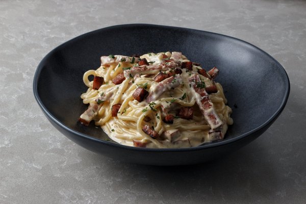 Creamy carbonara pasta with visible guanciale pieces in a dark bowl.