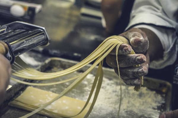 Hand-rolled fresh pasta ribbons being cut on a floured pasta machine.