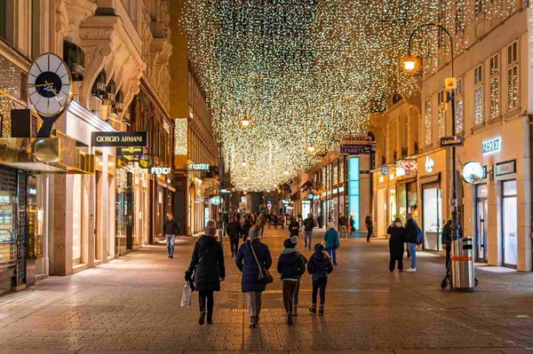 Strada commerciale decorata con luci natalizie e negozi di lusso, persone che passeggiano di sera.