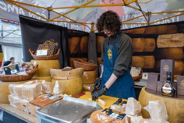 Venditore che taglia grandi forme di formaggio italiano stagionato a una bancarella di mercato.