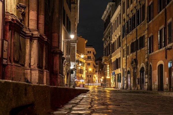 Stretta strada acciottolata a Roma illuminata da luci calde di notte.