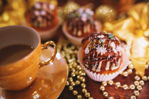 Tazza dorata con caffè accanto a dolci natalizi decorati con cioccolato e zuccherini, circondati da perline dorate.