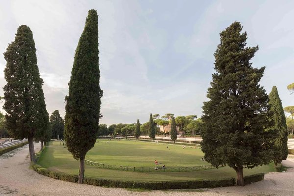 Giardini di Villa Borghese a Roma con alberi di cipresso e un ampio prato verde.