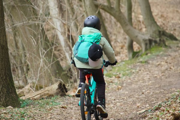 Bambino con il casco che pedala lungo un sentiero alberato.