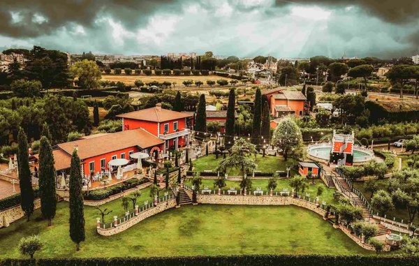 Vista panoramica di un'area verde con edifici rossi e alberi, sotto un cielo nuvoloso.