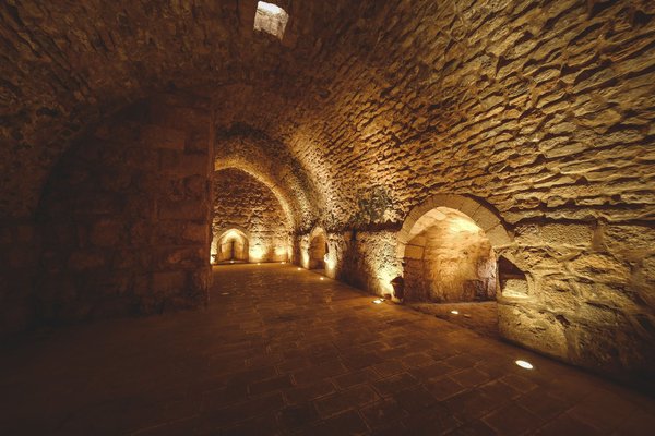 Camera sotterranea a volta in pietra illuminata da luci calde lungo le pareti.