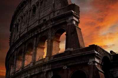 Close-up view of the Colosseum in Rome at sunset with an orange sky and highlighted architectural details.