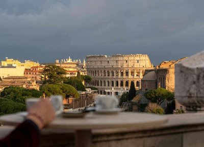 Panoramic view of Rome with the Colosseum at sunset and a coffee cup in the foreground.