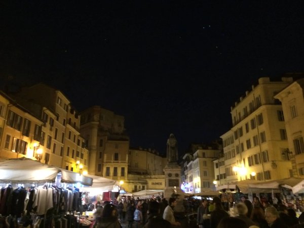 Mercato di Campo de' Fiori a Roma di notte con la statua di Giordano Bruno e bancarelle illuminate.