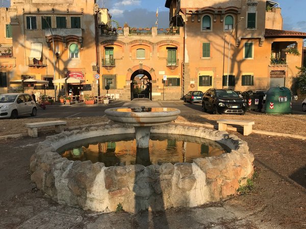 Fontana storica in Piazza Brin circondata da edifici con facciate in terracotta nel quartiere Garbatella di Roma.
