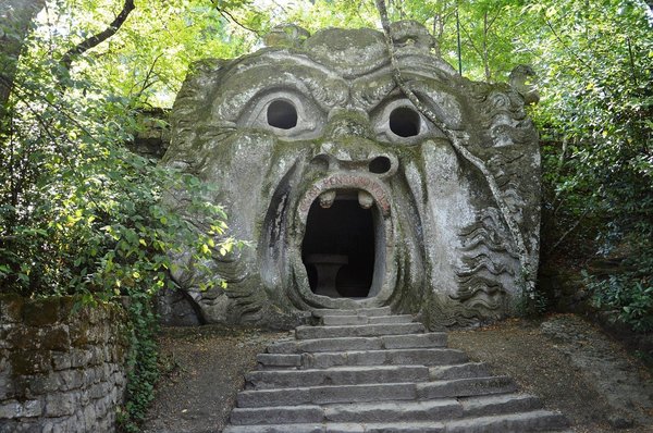 Scultura iconica della Bocca dell'Orco nel Parco dei Mostri di Bomarzo, circondata da vegetazione e scale in pietra.