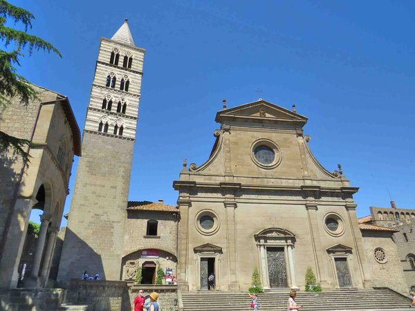Cathedral of San Lorenzo and bell tower in Viterbo on a sunny day, with a blue sky and visitors in the square.