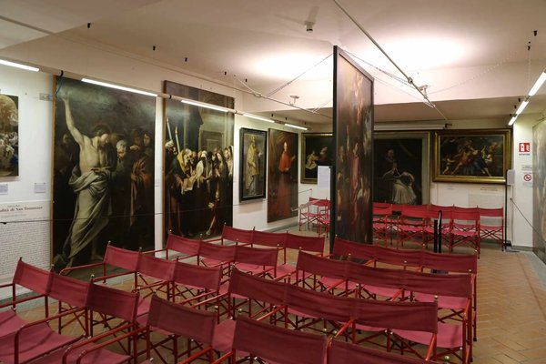 Interior of the Civic Museum of Viterbo with historical paintings and red chairs arranged for events.