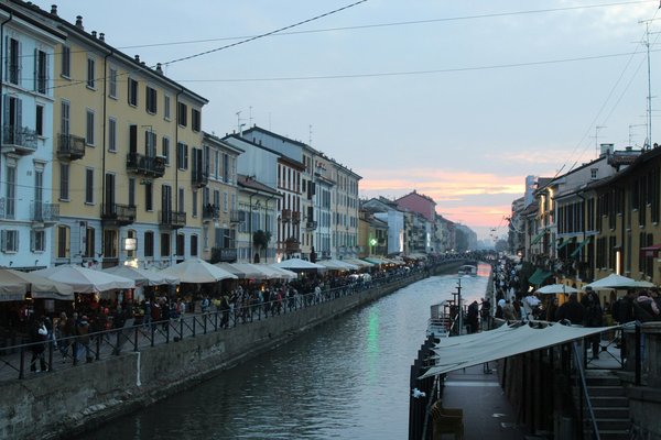 Vista serale dei Navigli di Milano con edifici colorati, canale e persone che passeggiano lungo le rive.