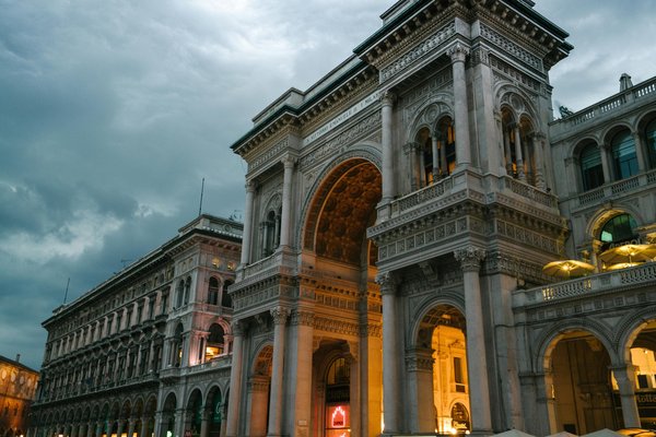 Ingresso illuminato della Galleria Vittorio Emanuele II a Milano con dettagli architettonici e cielo nuvoloso.