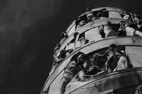 Scultura iconica del Cimitero Monumentale di Milano in bianco e nero, con dettagli intricati e cielo scuro sullo sfondo.