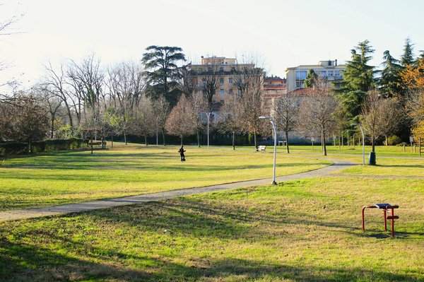 Parco con prati verdi, alberi spogli e edifici residenziali sullo sfondo a Milano.