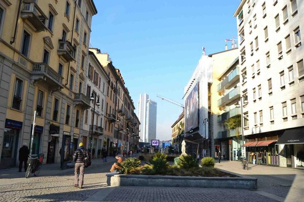 View of Corso Como in Milan with modern and traditional buildings, blue sky, and people strolling.