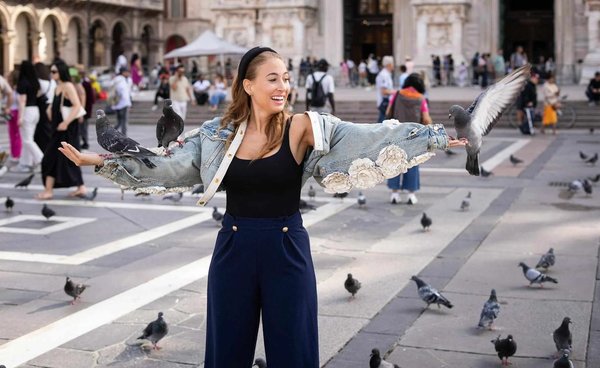 Woman with pigeons in Piazza del Duomo in Milan, with architectural details of the Duomo in the background.
