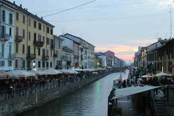 View of the Navigli district in Milan with a canal, colorful buildings, and an outdoor market at sunset.