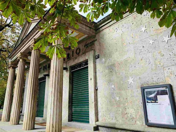 Facade of the Milan Planetarium with columns and star decorations, surrounded by green leaves.