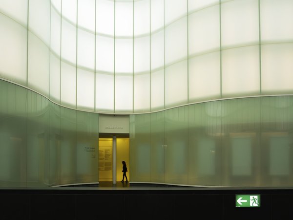 Translucent glass-panel courtyard of MUDEC, Milan's Museum of Cultures, with a visitor silhouetted in the entrance.