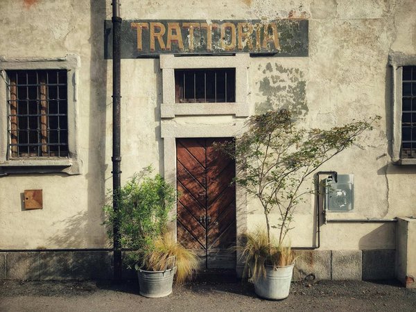 Facade of a traditional trattoria in Milan with wooden door and potted plants.