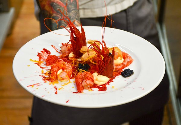 Fine-dining plate of raw red prawns elegantly arranged with caviar and citrus garnish.