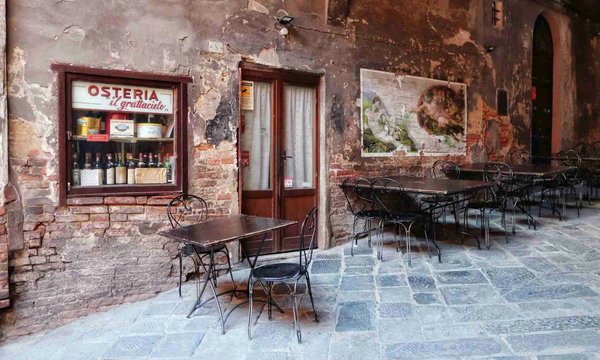 Rustic exterior of an osteria with wrought iron tables and chairs and exposed brick walls.