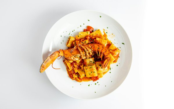 Italian pasta with lobster in tomato sauce on a minimalist white plate.