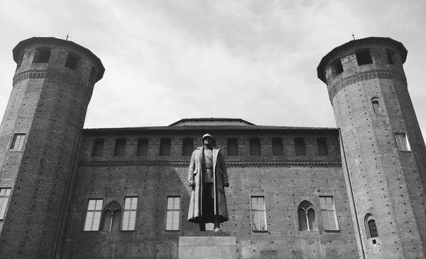Statua davanti a un edificio storico con torri in mattoni a Torino, in bianco e nero.