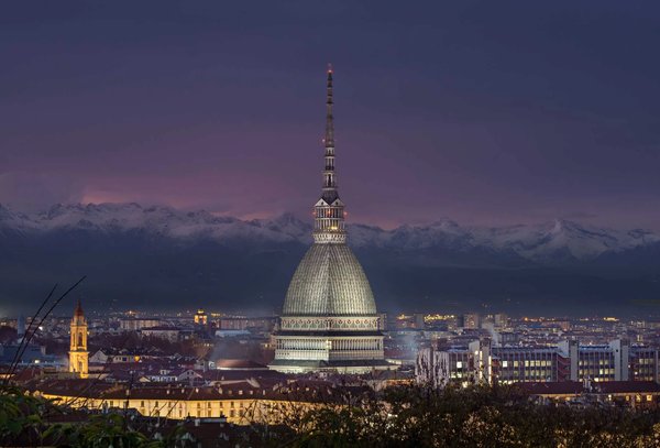 Vista notturna della Mole Antonelliana a Torino con le Alpi sullo sfondo e luci della città.