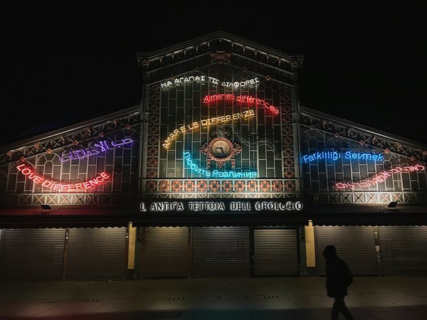Facciata illuminata della Tettoia dell'Orologio al mercato Porta Palazzo di Torino con scritte al neon colorate.