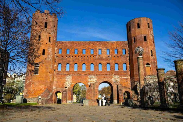 Porta Palatina a Torino con cielo blu e visitatori in primo piano, simbolo del Quadrilatero Romano.