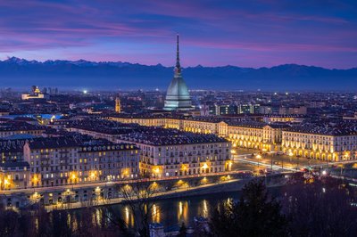 Vista notturna di Torino con la Mole Antonelliana illuminata e le Alpi sullo sfondo.