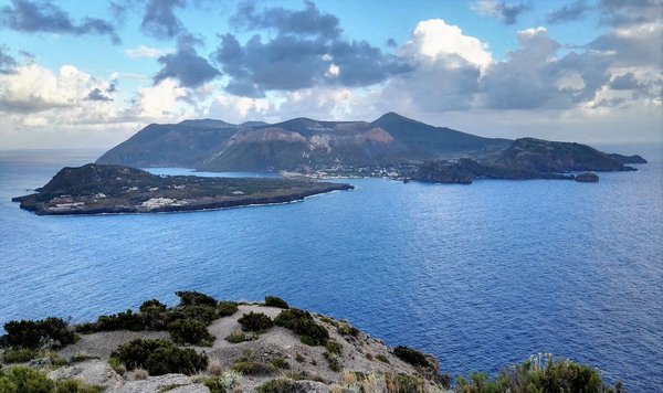 Panoramic view of the Aeolian Islands with volcanic landscape and blue sea under a partly cloudy sky.