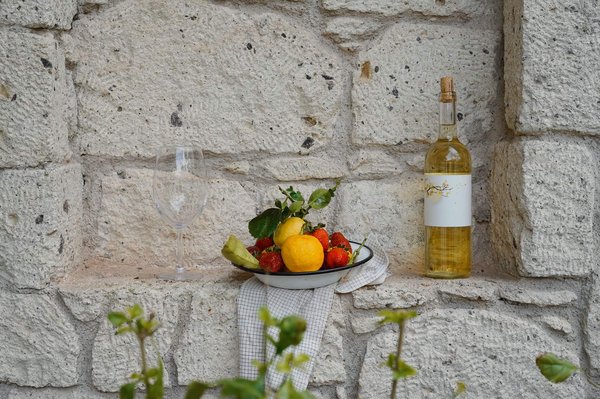 Malvasia wine bottle, empty glass, and fresh fruit against a rustic stone background.