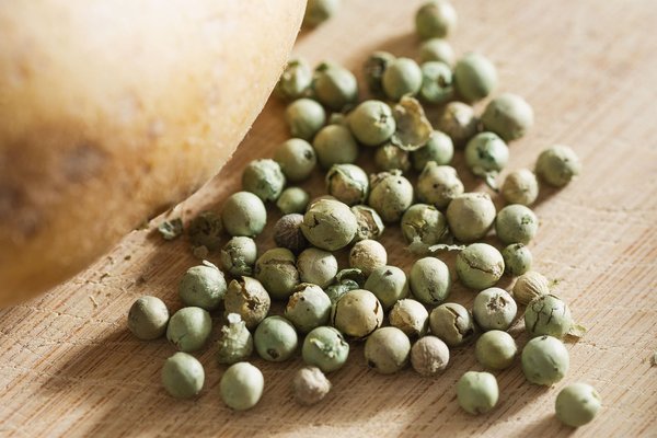 Close-up of green peppercorns and a potato on a wooden cutting board.