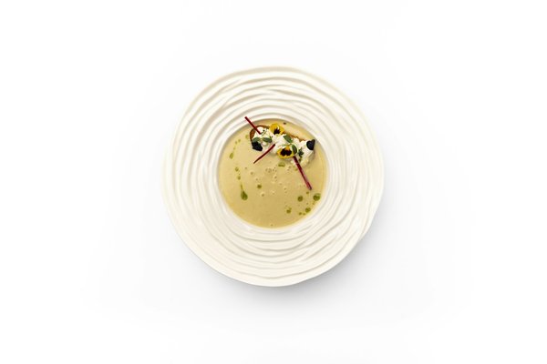Elegant pale-green veloute soup with edible flowers on a designer white plate.