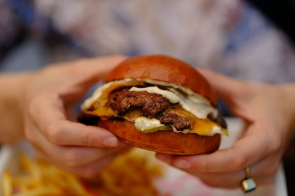 Gourmet burger with melted cheese and pickles in a brioche bun, held in hand.