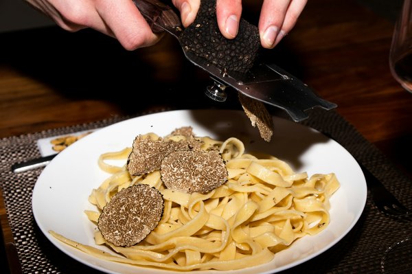 Fresh black truffle being shaved tableside onto a plate of tagliatelle pasta.
