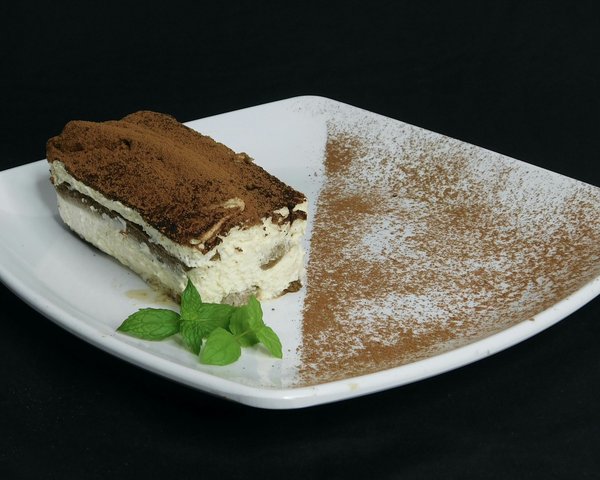 Slice of tiramisù dusted with cocoa powder and garnished with mint.