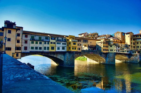 Vista del Ponte Vecchio a Firenze con riflessi sull'Arno in una giornata soleggiata.