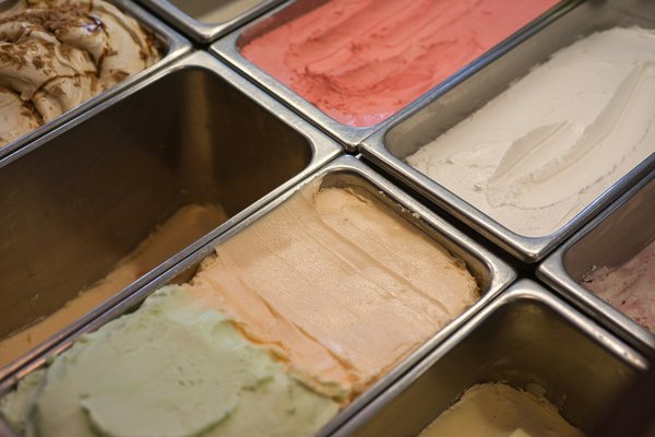 Primo piano di gusti di gelato, tra cui pistacchio e fragola, in vaschette metalliche.